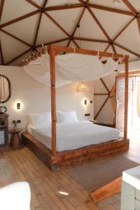 Geodesic dome-style hotel room with a wooden canopy bed, soft lighting, and minimalist rustic design featuring wood and woven textures.