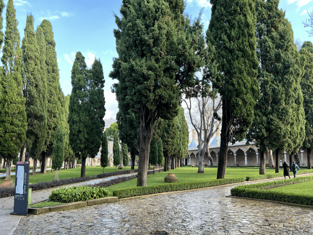 Lush green garden with tall cypress trees and stone paths in Topkapi Palace’s spacious Second Courtyard.