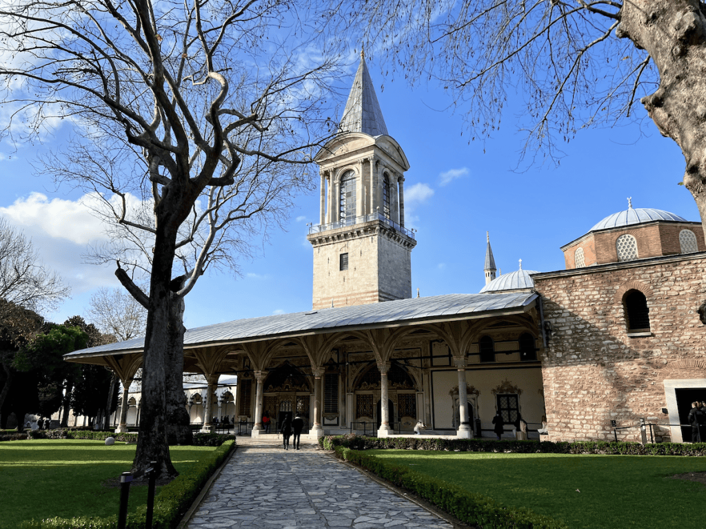 View of the Tower of Justice rising above a colonnaded hall inside the palace grounds, symbolizing Ottoman legal authority.