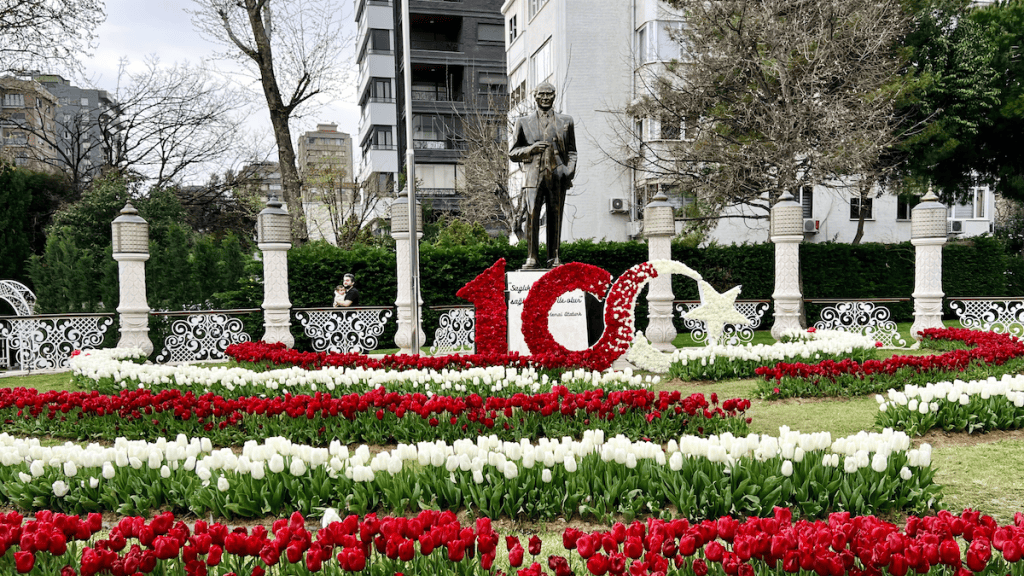 A large floral installation celebrating the Turkish Republic’s 100th anniversary with red and white tulips forming the number “100” and crescent-star, set in front of a statue of Atatürk.