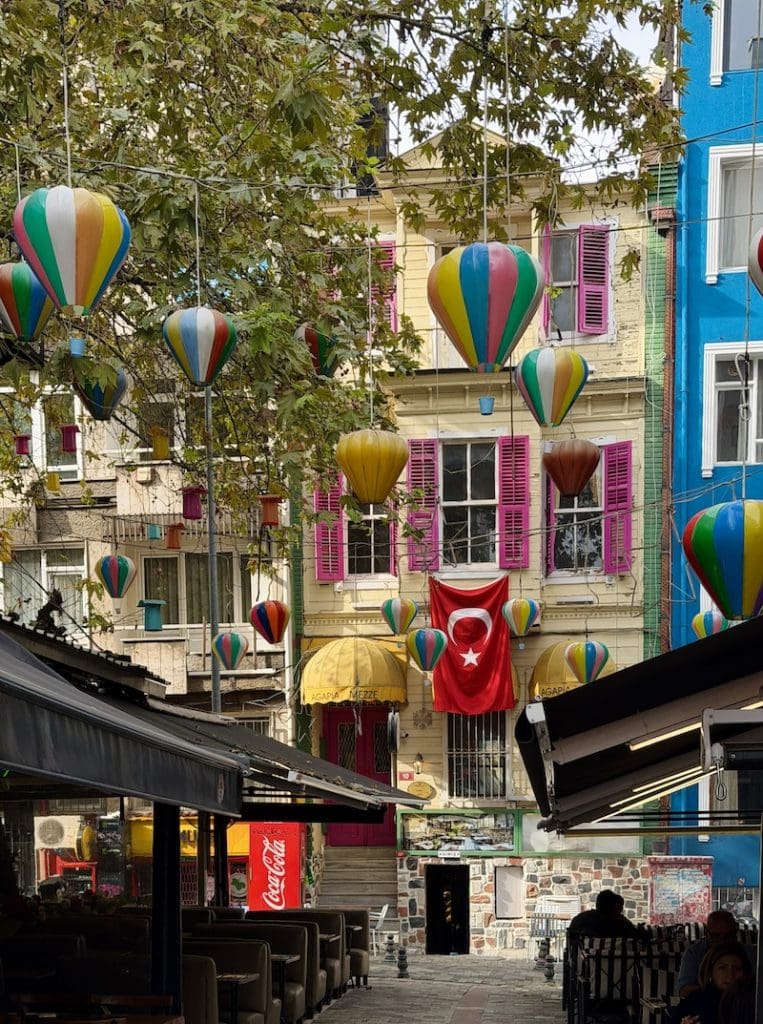 Colorful street in Istanbul decorated with hanging hot air balloon ornaments and a Turkish flag between pastel buildings