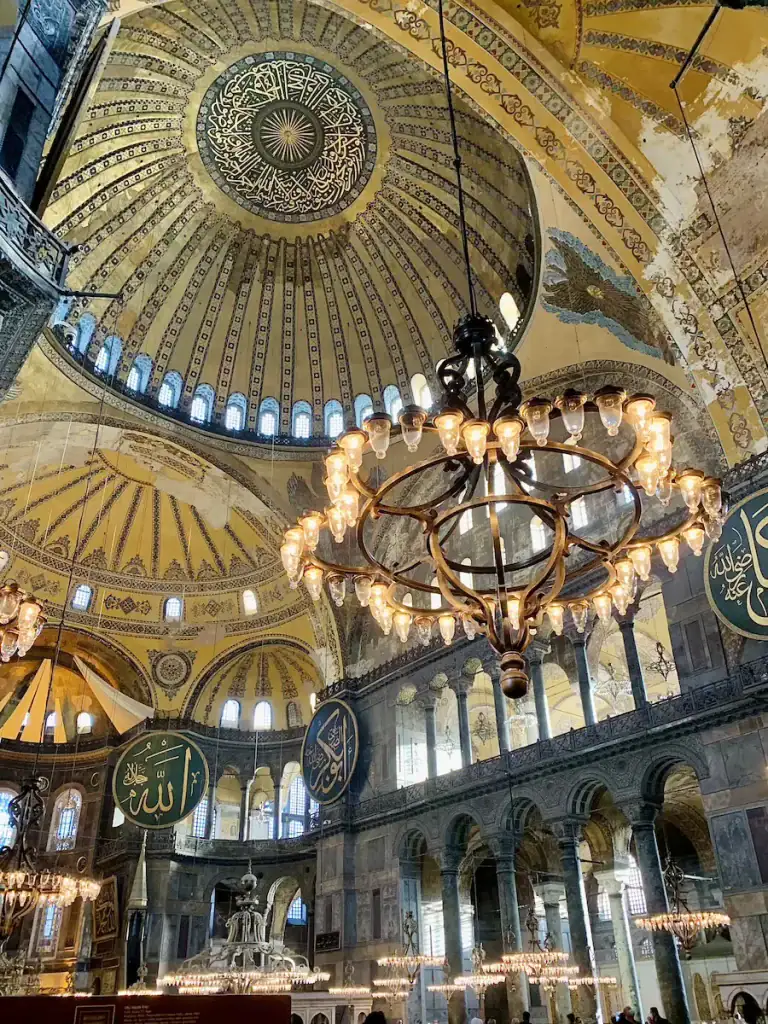 Interior of Hagia Sophia in Istanbul with a massive golden dome ornate chandeliers and circular Arabic calligraphy medallions