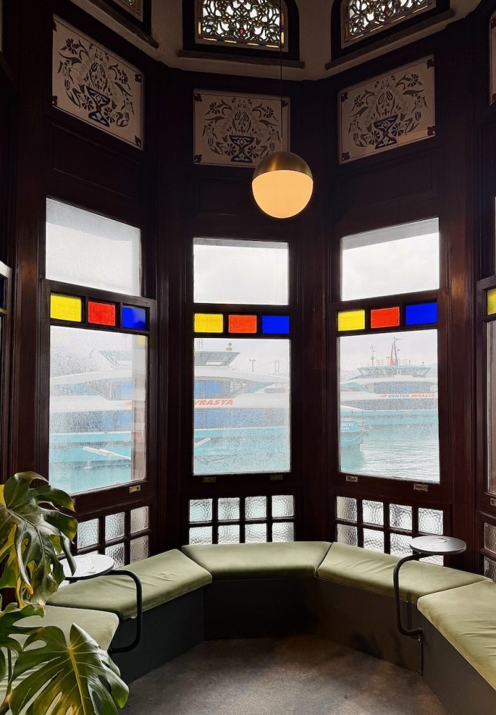 Ottoman-style ferry terminal room in Besiktas with stained-glass windows and cushioned seating overlooking boats on the Bosphorus.