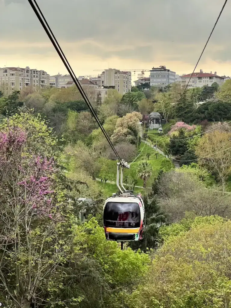 Cable car gliding over lush green hills with city buildings in the distance near Macka Park in Besiktas, showing one of the area’s scenic viewpoints.