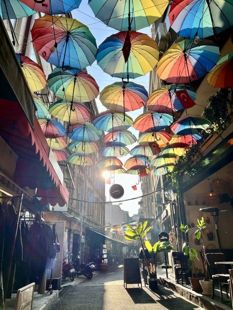 Colorful umbrellas hanging overhead on a narrow side street in Galata filled with cafes and boutiques.