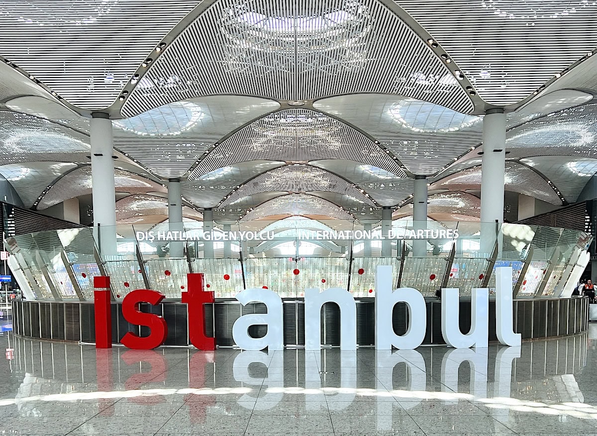 Large open terminal hall inside Istanbul Airport with a curved patterned ceiling and large red and white letters spelling "istanbul" near the international departures area.